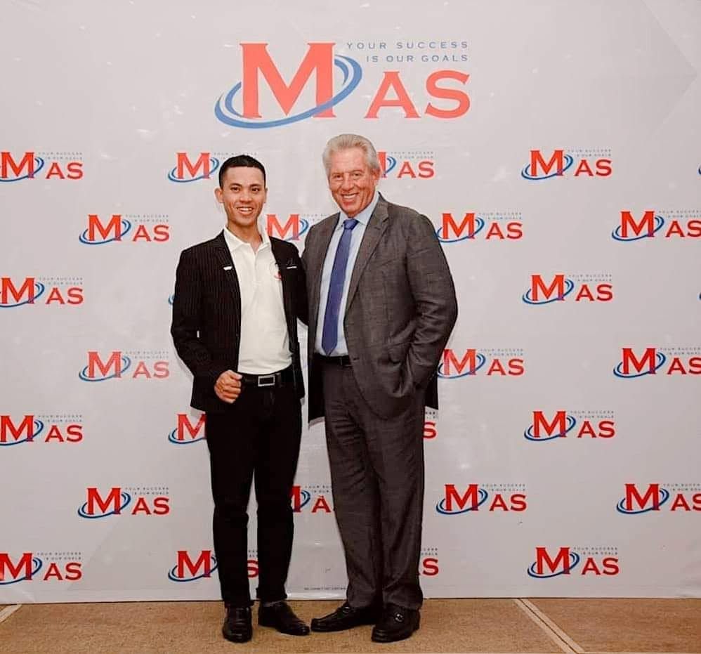 Lê Văn Cương đứng chụp ảnh cùng John C. Maxwell trước backdrop sự kiện MAS