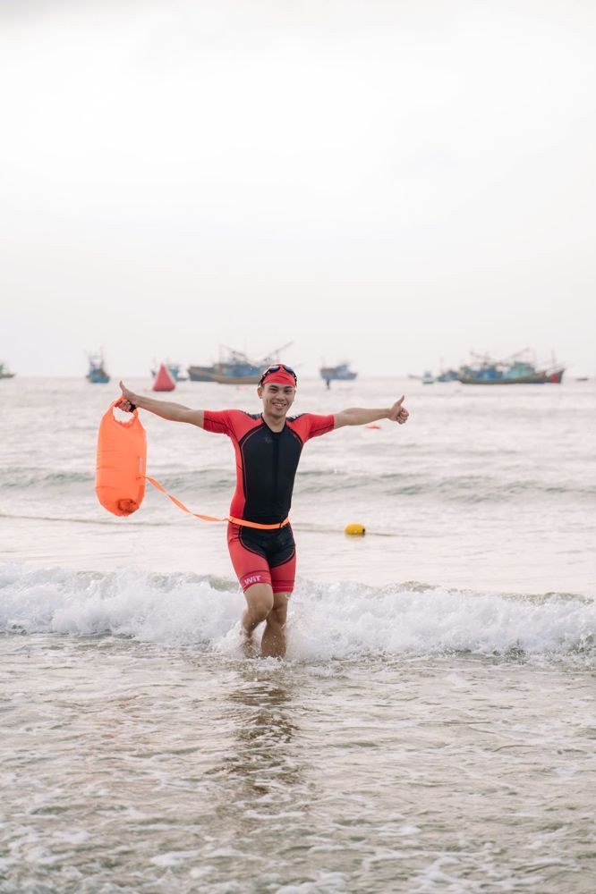 Lê Văn Cương trong trang phục bơi, dang tay bước lên từ biển, kéo theo phao bơi màu cam