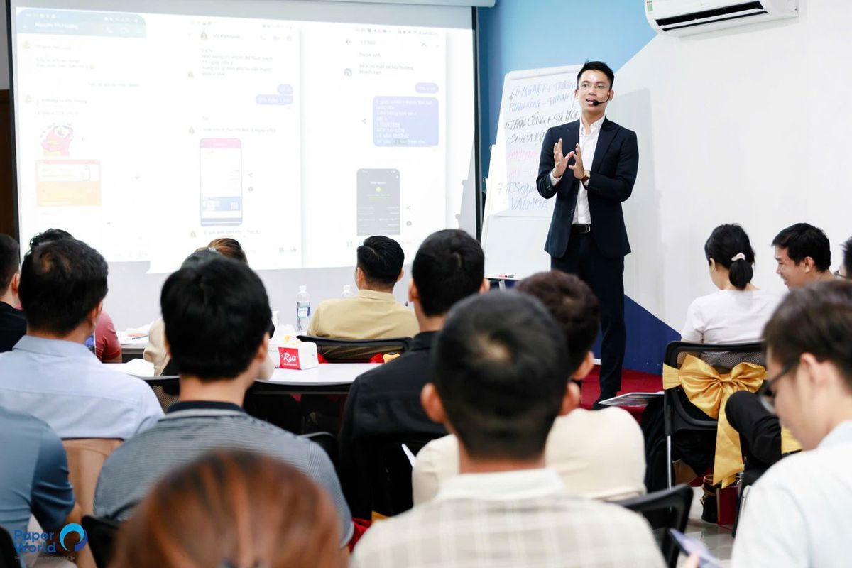 Lê Văn Cương đeo micro cài tai, đứng lớp trước học viên trong phòng học có màn chiếu