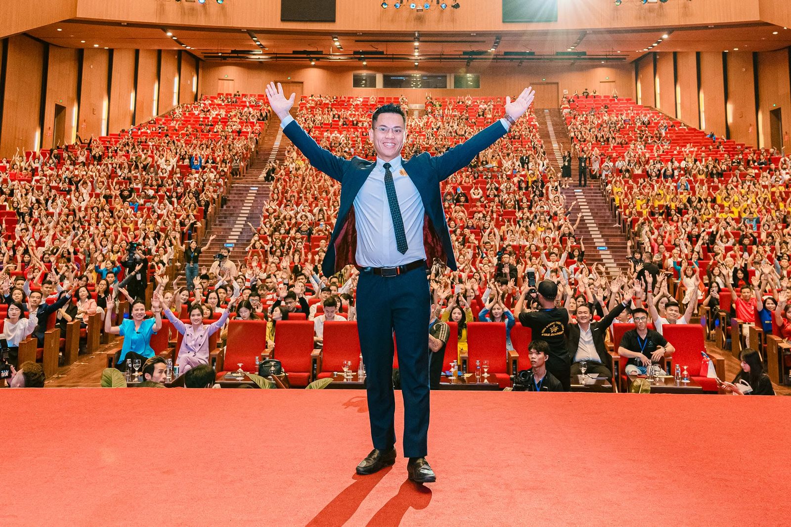 Lê Văn Cương đứng giữa sân khấu, dang hai tay trước khán phòng kín chỗ đang giơ tay hưởng ứng